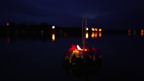 Loy-Krathong-Festival:-Big-Beautiful-Krathong-with-a-burning-candle-and-incense-on-top-made-from-banana-leaves-and-orange-flowers-on-the-dark-blue-water-at-night