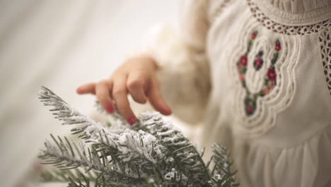 Slow-motion-shot-of-Young-girl-caressing-Pine-Christmas-Ornament-Branch-in-white-festive-dress---Close-up