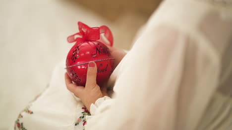 Over-the-shoulder-of-kid-in-a-Christmas-white-dress-holding-a-red-bauble---close-up-shot