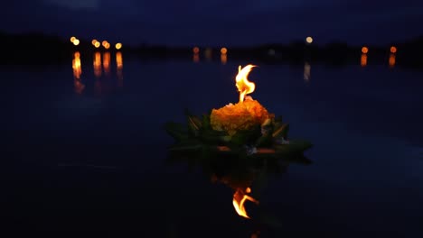 Loy-Krathong-Festival:-Beautiful-Krathong-made-from-banana-leaves-and-orange-flowers-with-a-burning-candle-top-on-the-dark-blue-water