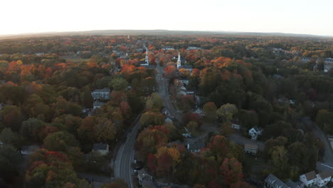 Drone-shot-of-small-town-among-colorful-autumn-trees-at-sunset