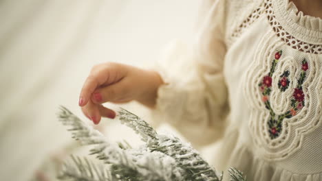 Young-girl-caressing-Pine-Christmas-Ornament-Branch-in-white-festive-dress---Close-up