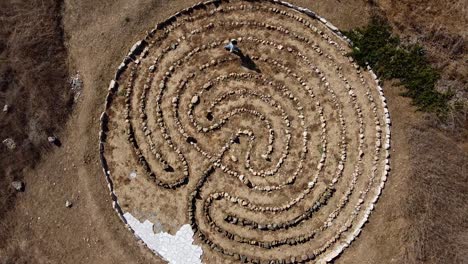 Aerial-view-of-a-person-walking-through-a-stone-maze-art-installation,-Finding-the-Future-in-Avdimou-Beach