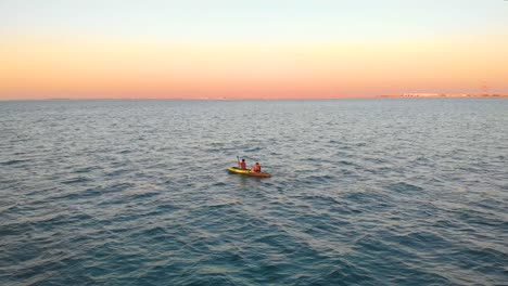 A-Couple-Paddle-in-a-Kayak-across-the-Middle-Eastern-Ocean-during-an-Amazing-Sunset,-Drone-Aerial