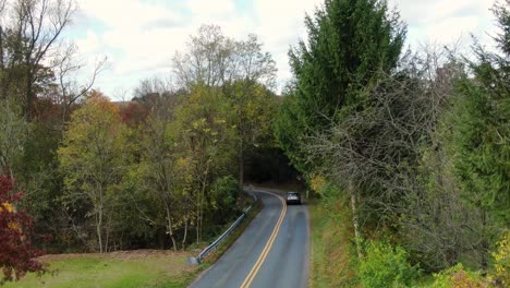 Small-Sport-Utility-Vehicle-SUV-driving-down-winding-hill-into-woods-during-autumn