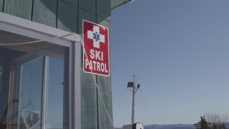 Ski-patrol-red-sign-posted-on-the-exterior-wall-of-a-cabin,-clear-day