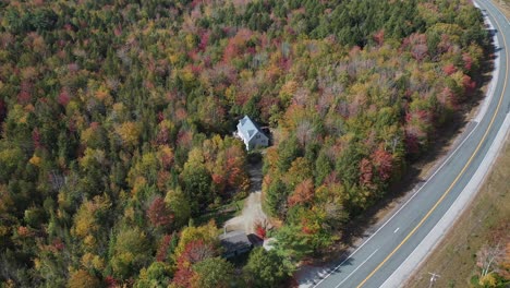 Vista-Aérea-De-La-Autopista-Y-Casa-Aislada-En-Un-Bosque-Colorido-En-Un-Día-Soleado-De-Otoño-En-El-Campo-De-Nueva-Inglaterra,-Maine-Usa,-Disparo-De-Drones