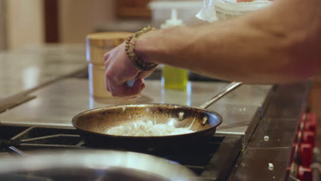Man-sprinkling-handful-of-cheese-over-frying-pan-in-slow-motion