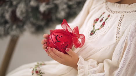 Slow-motion-shot-of-Young-girl-in-a-Christmas-ornamented-white-dress-holding-a-red-bauble---close-up