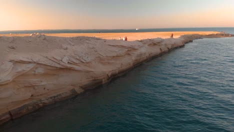 Nahöstliche-Männer,-Die-Kanduras-Tragen,-Gehen-Während-Des-Sonnenuntergangs-über-Die-Unglaublich-Erodierte-Küste-Von-Abu-Dhabi-Am-Persischen-Golf