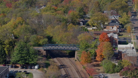 Railroad-tracks-and-bridge-in-Kirkwood,-Missouri-on-a-beautiful-Fall-day-with-a-tilt-down-to-reveal-train-station