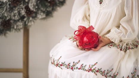 Zeitlupenaufnahme-Eines-Mädchens-In-Einem-Festlichen-Weihnachtskleid,-Das-Eine-Rote-Zierkugel-Hält