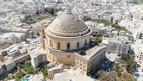 Far-view,-aerial-4k-drone-footage,-circling-the-Mosta-Rotunda-Dome,-a-Roman-Catholic-church,-and-the-surrounding-city-of-Malta