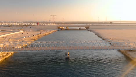 Drone-flies-over-epic-iron-bridge-in-Barren-Abu-Dhabi-setting-during-sunset,-Aerial