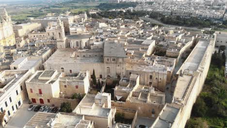 Historic-cityscape-of-Mdina,-overlooking-St-Paul's-Cathedral---Aerial-Upward-Reveal-Shot