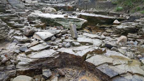 Broken-rough-wet-stone-pathway-cascading-rainfall-overcast-Autumn-hiking-trail