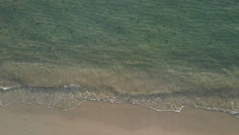 Aerial-top-view,-medium-slow-ascending-shot-of-ocean-small-tropical-wave’s-break-on-a-beach