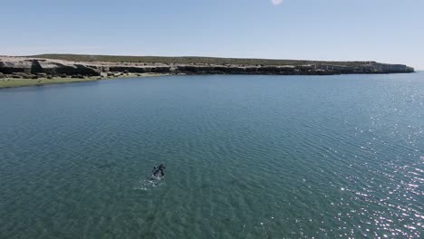 Two-People-Swimming-On-Deep-Blue-Crystal-Water-Near-Rocky-Coastline-Through-Sunny-Day-At-Villarino-Beach