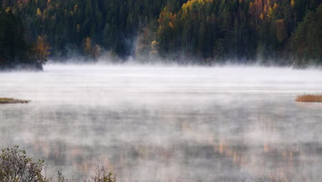 Mystical-fog-rolling-over-alpine-lake-in-autumn-forest,-Timelapse