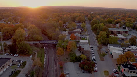 Aerial-push-over-train-tracks-and-train-station-and-main-street-of-charming-small-town-in-Autumn-at-sunset-on-a-beautiful-evening,-clip-two-of-two-continuous-clips