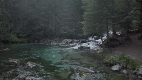 Kleine-Wasserfälle,-Die-In-Einen-See-Mit-Wald-Im-Hintergrund-Fallen