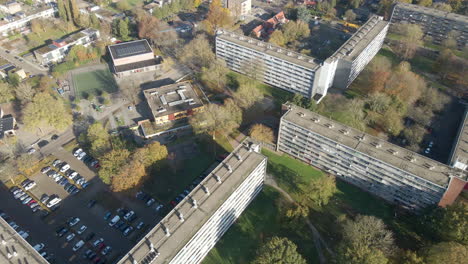 Aerial-overview-of-social-housing-flat-with-parking-lot-and-green-park-in-autumn