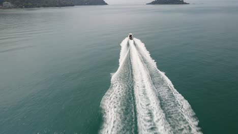 Aerial-drone-follow-shot-of-a-speed-boat-traveling-fast-towards-an-Island-in-a-tropical-sea-with-mountain-coastline