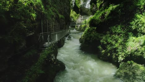 Drone-dolly-in-of-a-tumultuous-river-in-a-narrow-canyon-with-walkway