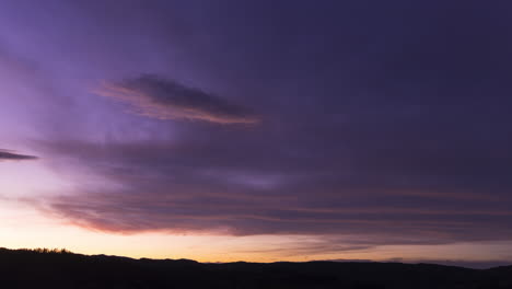 Dark-purple-and-blue-clouds-glow-with-sunset-light-in-sky,-Timelapse