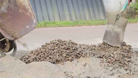 Dumping-rocks-gravel-into-the-cement-mixture-from-the-wheelbarrow-to-create-a-concrete-mixture-in-the-streets
