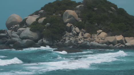 Slow-motion-shot-of-blue-water-crashing-against-rocks-in-an-island,-taken-in-Tayrona-Park,-Colombia,-South-America