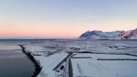 Hermosa-Puesta-De-Sol-Aérea-Sobre-Una-Montaña-Nevada-Y-El-Mar-Durante-El-Invierno