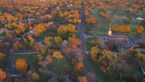 Flyover-charming-small-town-street-in-Ladue,-Missouri-near-a-church-and-with-a-lot-of-trees-in-Autumn-at-sunset