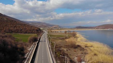 Lake-landscape,-panoramic-road-through-shore-and-hills-on-a-cloudy-day-in-Albania