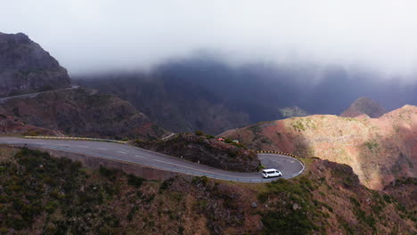 Spectacular-Aerial-tracking-shot-of-van-driving-on-dangerous-curvy-serpentines-road-in-mountains-during-foggy-day