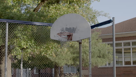 Low-angle-view-of-an-old-basketball-hoop-and-backboard-against-a-fence-on-an-elementary-school-playground