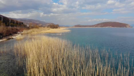Paradiesische-Seenlandschaft,-Kieselsteine-Am-Ufer-Und-Trockenes-Schilf,-Das-Von-Türkisfarbenem-Wasser-Umspült-Wird