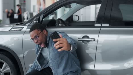 A-black-man-happily-shoots-a-video-near-the-car-in-a-car-dealership