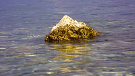 Golden-rock-washed-by-lake-water-on-a-sunny-beautiful-day-in-twilight