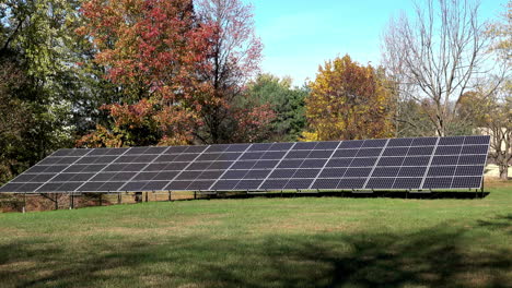 Long-shot-of-solar-panels-on-grassy-lawn-with-autumn-trees-in-background