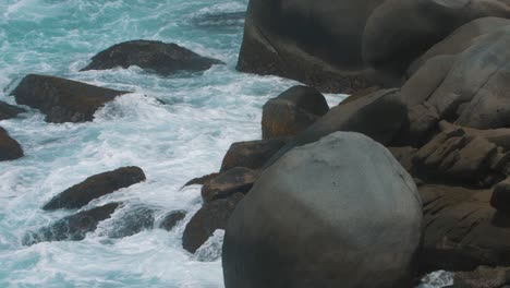 foamy-waves-of-water-crashing-against-rocks-on-the-beach-in-slow-motion-in-Tayrona-Park,-Colombia