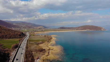 Cars-driving-on-panoramic-road-alongside-lake-shore-on-a-spring-beautiful-day