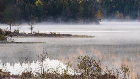 Mist-evaporating-off-tranquil-lake-in-autumn-forest,-Timelapse