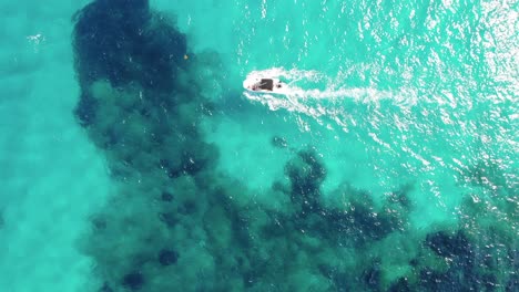 Rising-vertical-aerial-tracks-boat-motoring-over-reef-in-clear-water