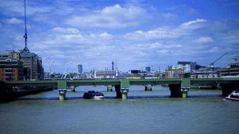 View-from-London-Bridge,-ferry-slowly-passes-under-adjacent-railway-bridge-on-a-sunny-day