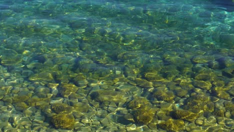 Colorful-bottom-of-lake-with-pebbles-reflecting-sunrays-on-turquoise-transparent-water