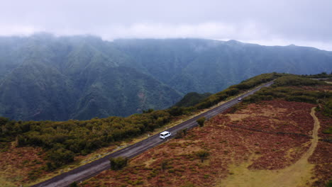 Drone-tracking-shot-of-white-van-driving-on-mountain-road-with-spectacular-hills-in-background