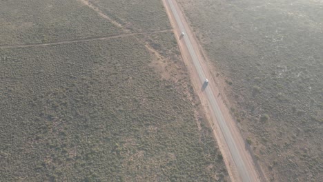 Car-driving-over-rural-road-in-the-australian-desert-with-a-long-shadow-during-golden-hour-In-Exmouth,-Western-Australia