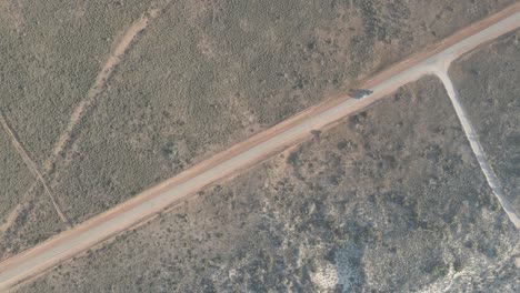 Car-driving-over-a-road-in-the-australian-desert-with-a-long-shadow-during-golden-hour-In-Exmouth,-Western-Australia