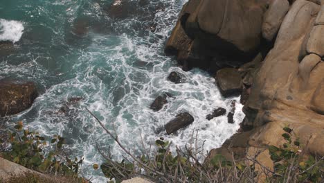 Waves-crashing-against-rocks-in-a-cliff-from-above-in-slow-motion,-taken-in-Tayrona-Park,-Colombia